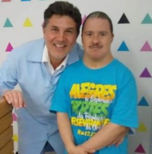 À esquerda, José Muniz com jaleco branco olha com sorriso para a foto, ao lado, paciente especial adulto, pós-atendimento odontológico no Instituto José Muniz.